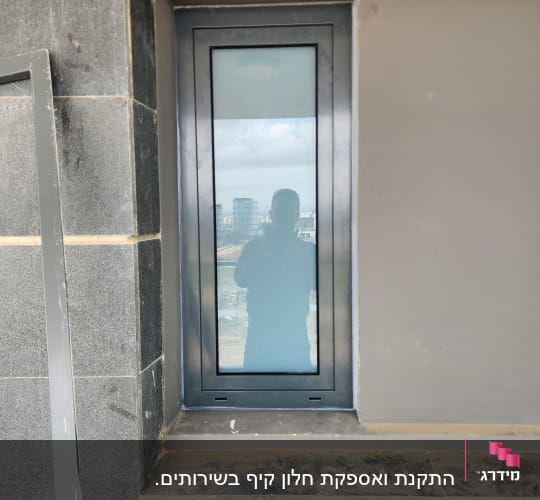 חלון אלומיניום צר במסגרת כהה על קיר אבן